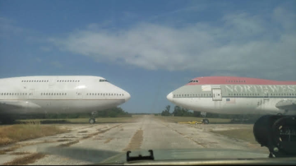 Two parked Boeing 747s facing each other wingtip to wingtip across a taxiway